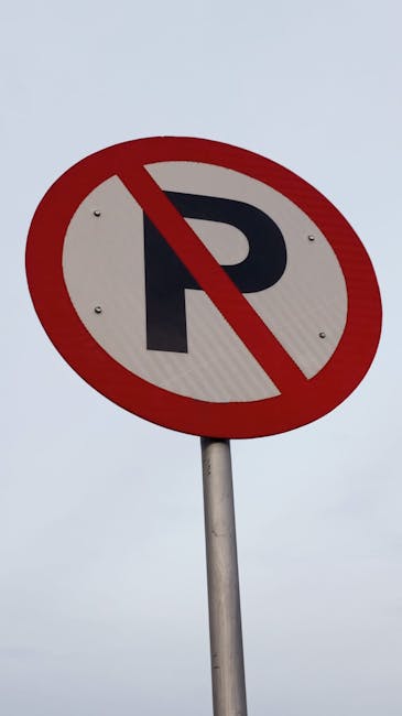 Close-up of a round 'no parking' sign with a red border and diagonal line crossing out the black letter 'P' on a light grey background, mounted on a metal pole. The image is taken outdoors under an overcast sky. This type of signage is important for indicating restricted parking areas in residential zones, often relevant for house removals and furniture transport during home relocation or moving services, as provided by Haringey Man and Van. Proper understanding of parking restrictions can facilitate efficient loading and unloading processes for professional removals teams, helping to comply with local council rules for parking permits in Haringey. The sign's clear visibility ensures drivers and movers are aware of no-parking zones, aiding in planning the logistics of household moves while minimizing delays and parking violations.